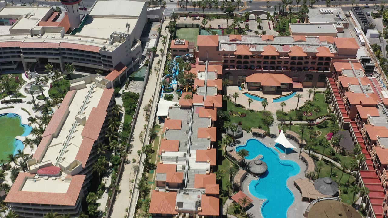 High-angle view of the San Jose del Cabo resort centered on curved blue pools, red-roofed lodging blocks, landscaped lawns, and no visible people.