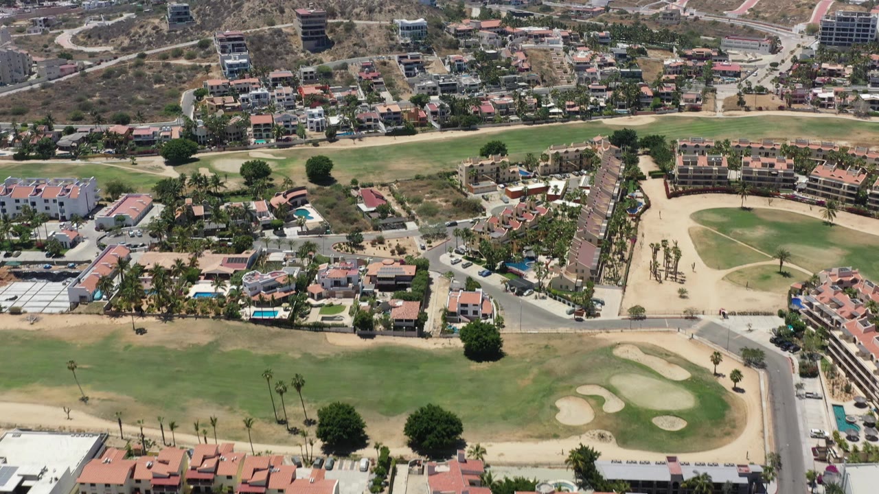 Aerial view of a golf green, sand traps, houses, roads, and hills.