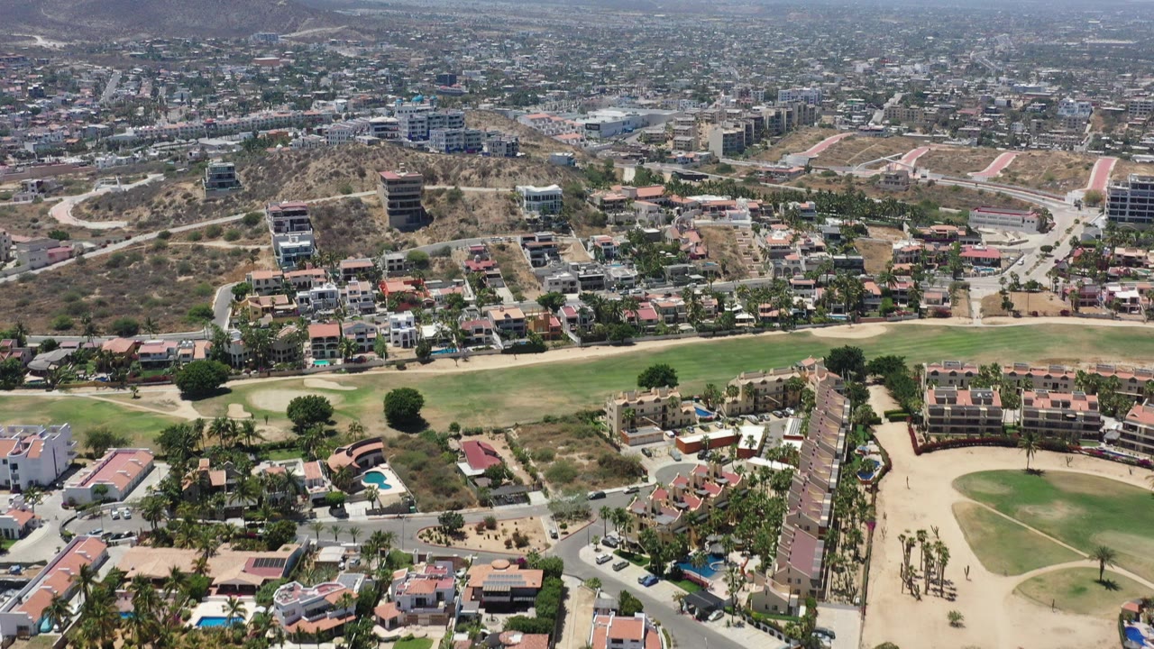 Aerial view of hillside homes, roads, green fields, and distant city blocks.