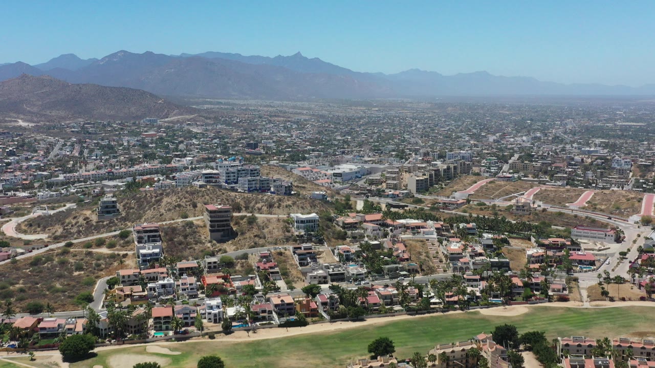 Aerial view over hillside homes, roads, and distant mountains.