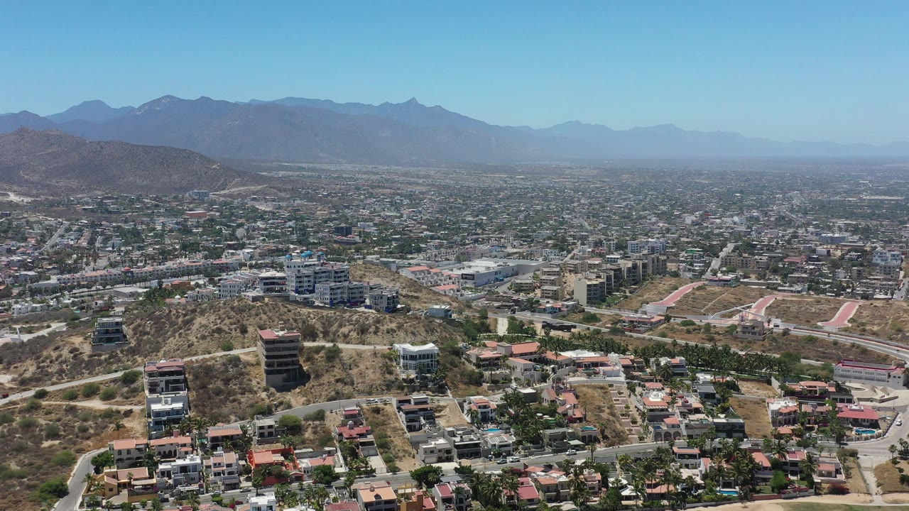 Aerial city view with hillside residences, roads, and a long mountain ridge.