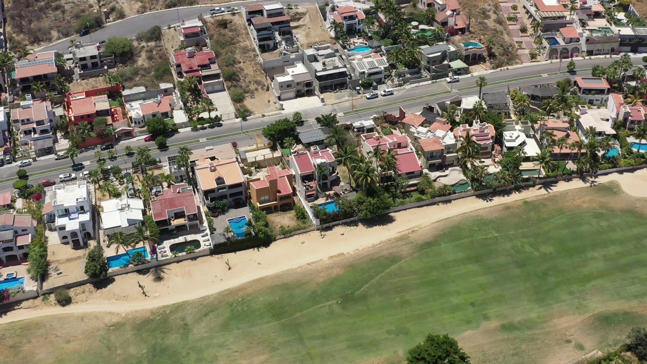 Overhead residential coastline with pools, road, sand, and green ground.
