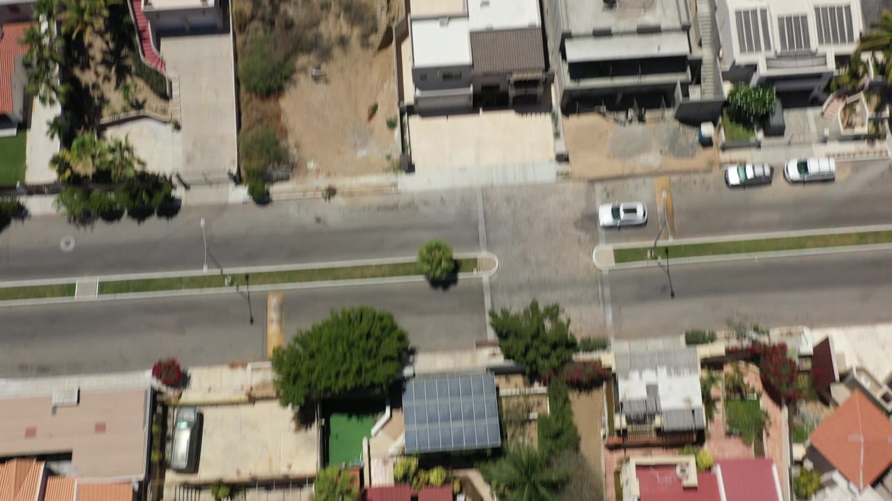 Aerial view of houses along a quiet paved street with cars nearby.