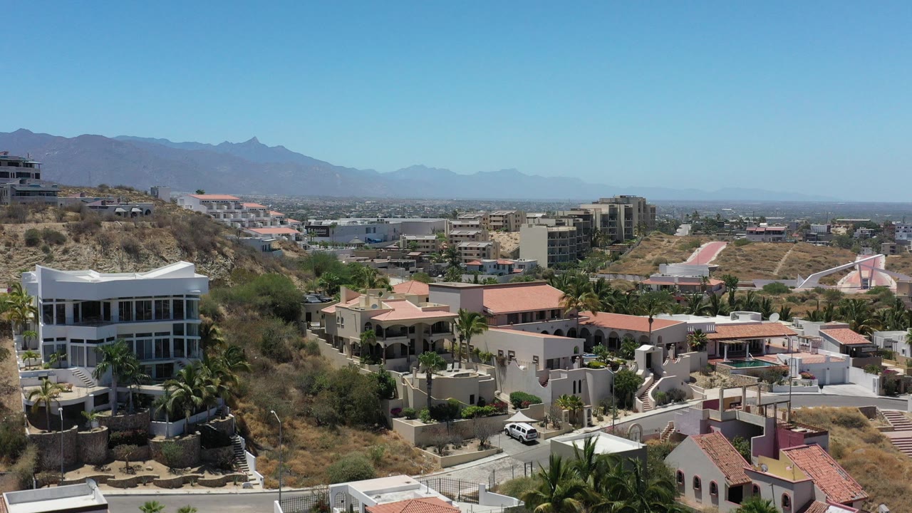 Aerial view of hillside homes, palms, and distant mountains.