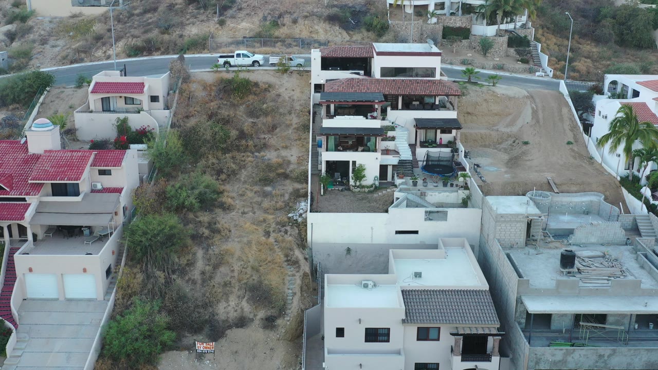 Elevated view in San Jose del Cabo of white homes with red tile roofs beside a dry hillside and a curved road, with no visible people.
