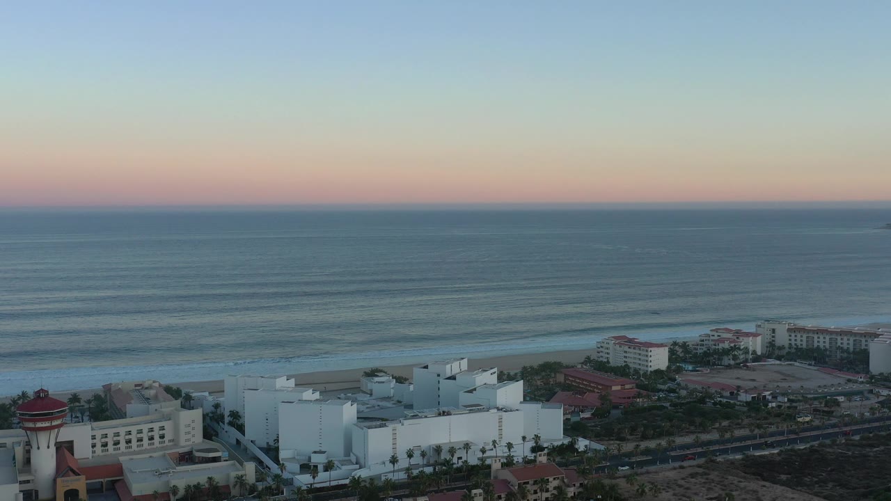 Pastel sunrise sky over calm sea and beachfront buildings.