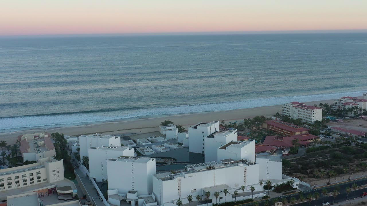 Beach resort complex below a calm ocean and pink horizon.
