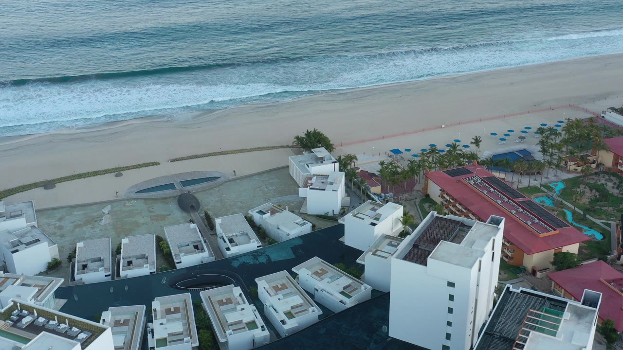 Beachfront resort rooftops with a red hotel wing and ocean waves beyond.