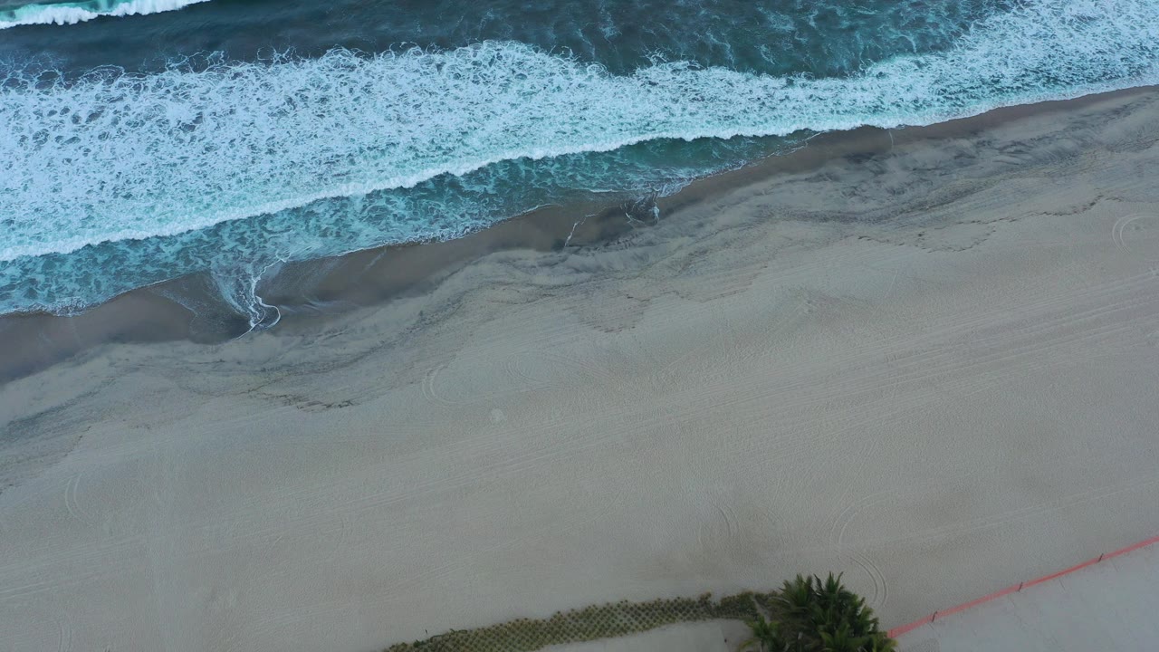 Overhead waves breaking onto pale sand.