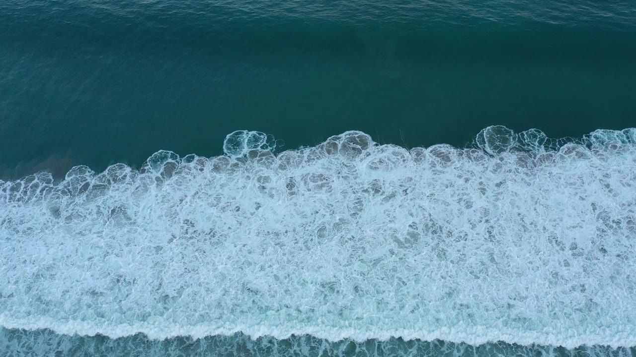 Dense white wave foam crosses the upper part of teal ocean water.