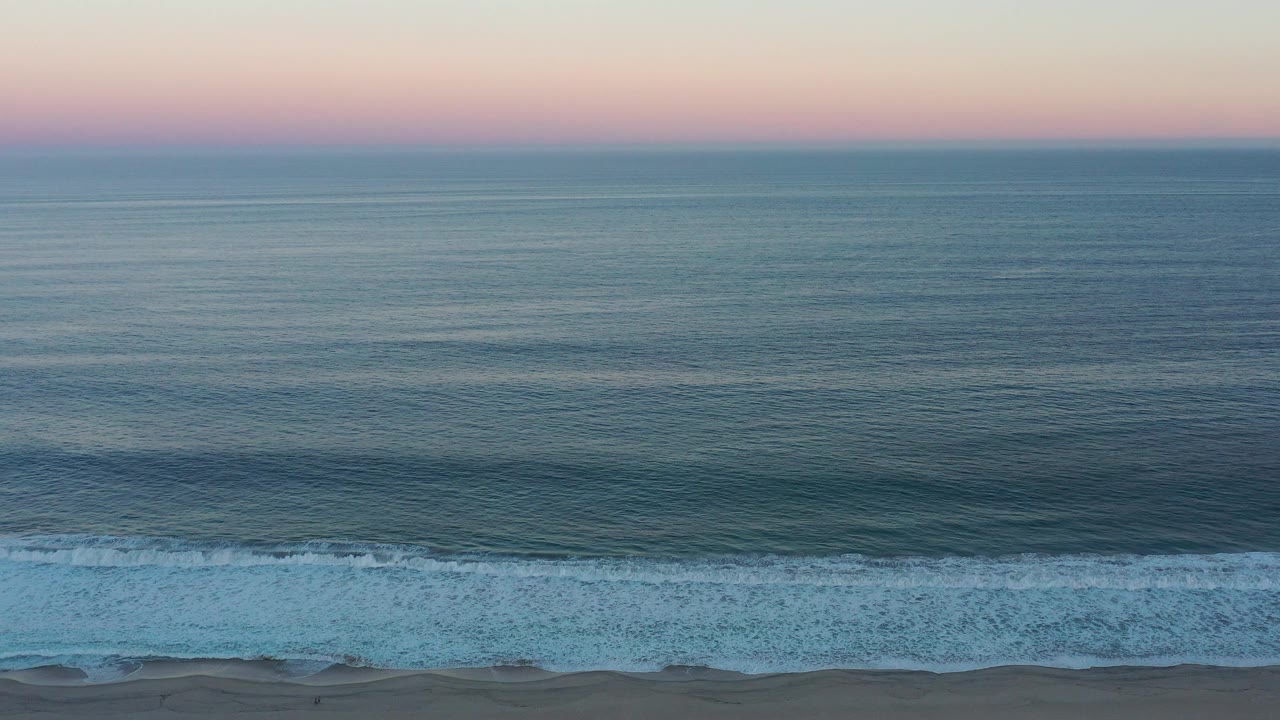 White surf rolls toward a narrow sandy shoreline at dusk