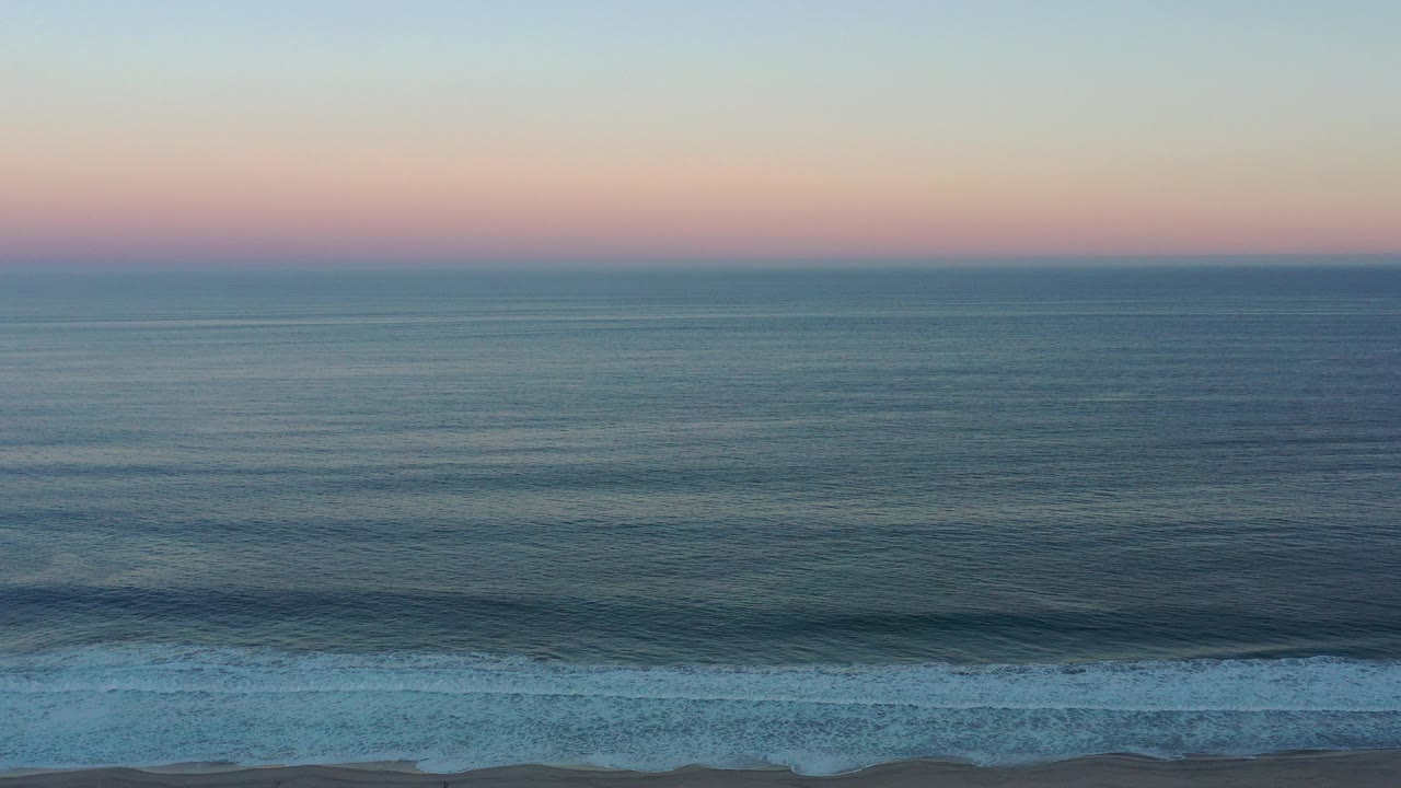 Wide ocean horizon above low surf at sunset.