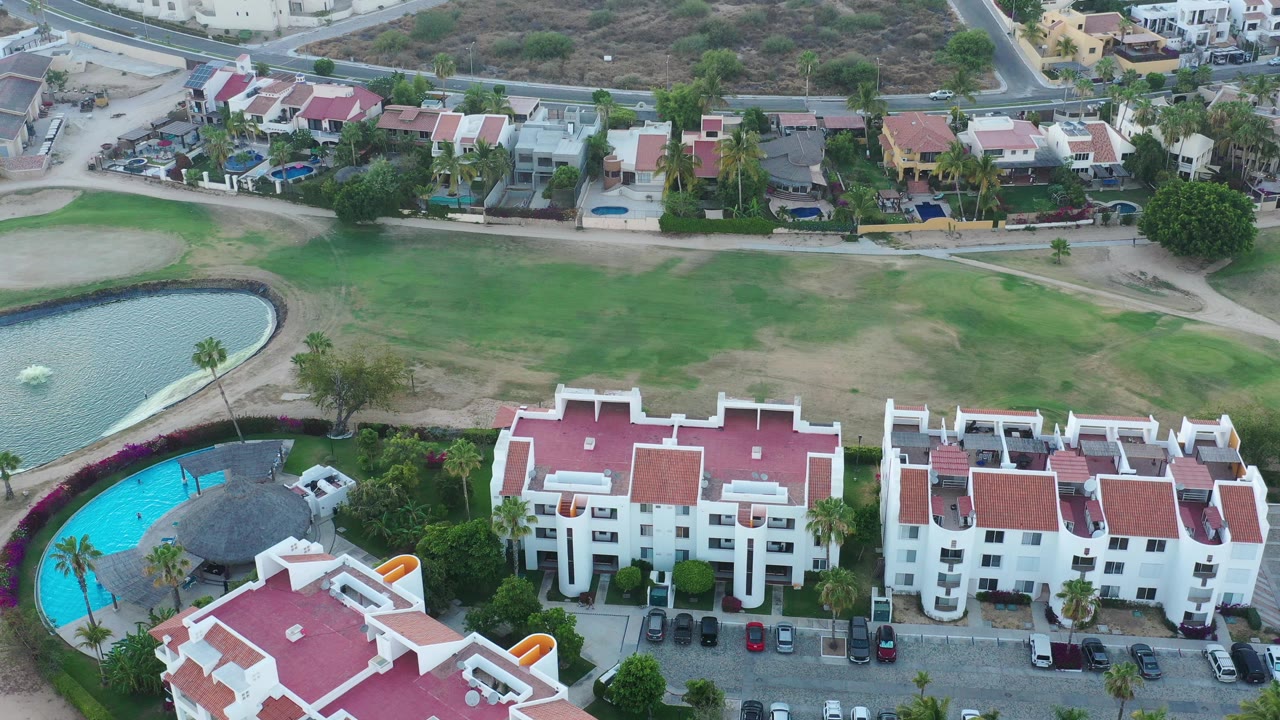 Overhead view of white residences beside lawns, pond, and pool.