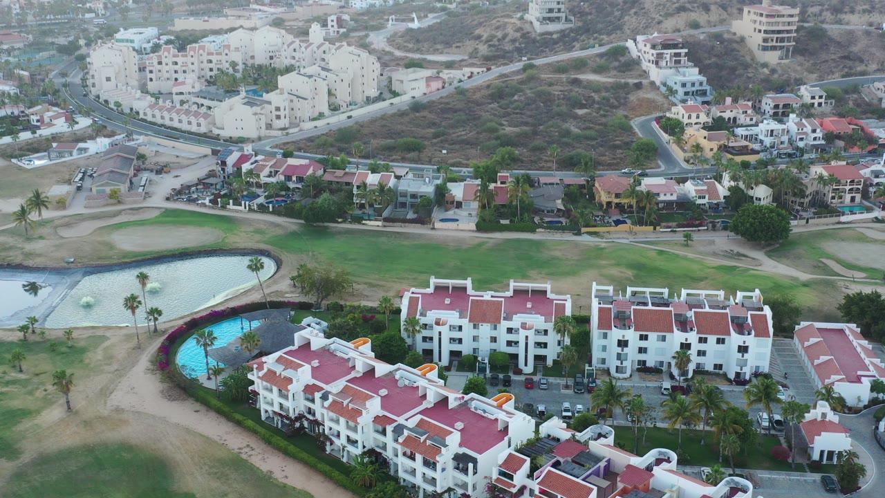 Aerial view of red-roofed buildings, green grounds, roads, and pools below a hillside town.