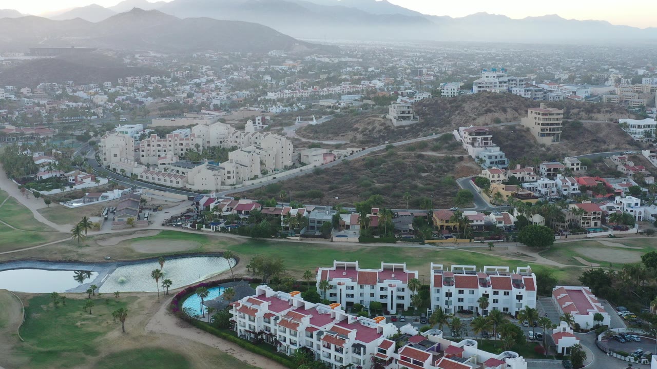 Aerial view over red-roofed homes, ponds, and mountains at low light.
