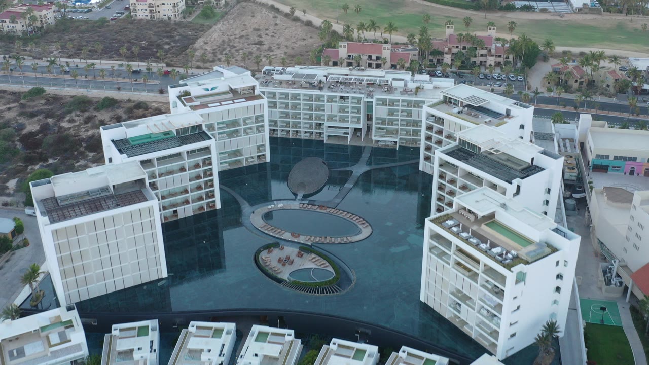 Aerial view of white hotel buildings around a dark pool courtyard