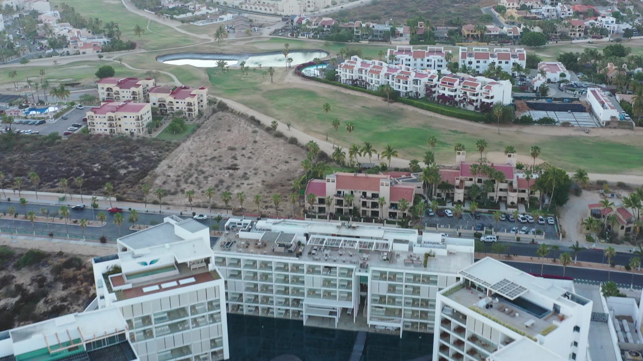 Aerial view of white residential buildings near a golf course and hillside homes.