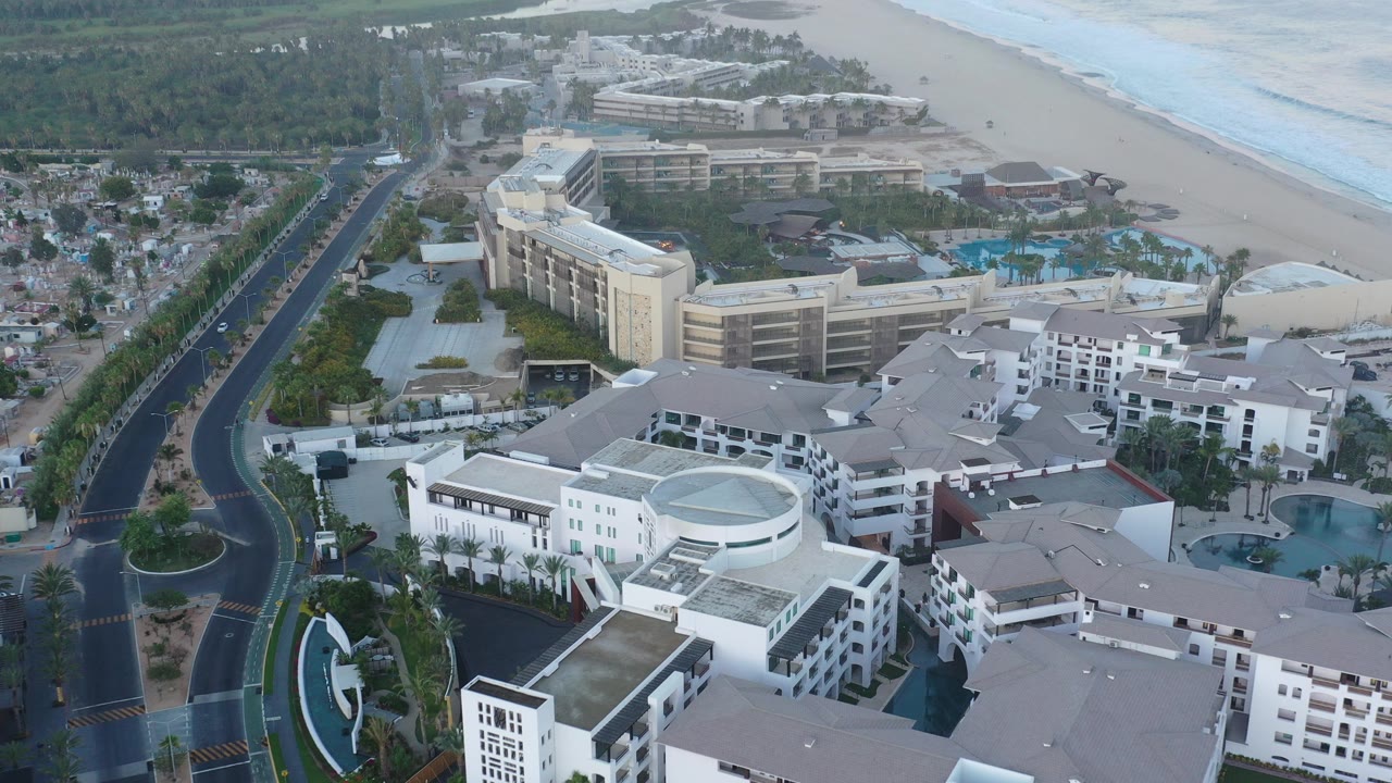 Aerial view of resort buildings, road, beach, and ocean surf.