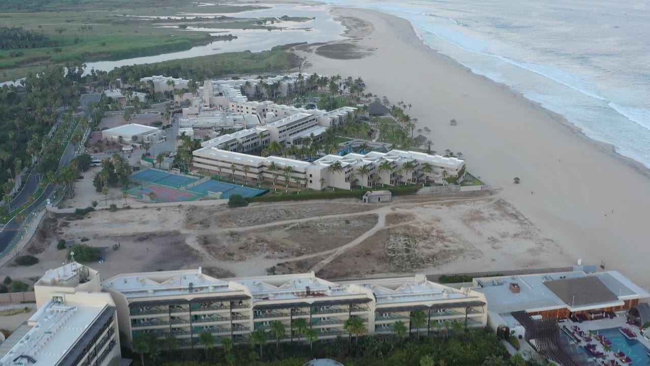 Aerial coastline view with white buildings, tennis courts, beach, ocean, and wetlands.