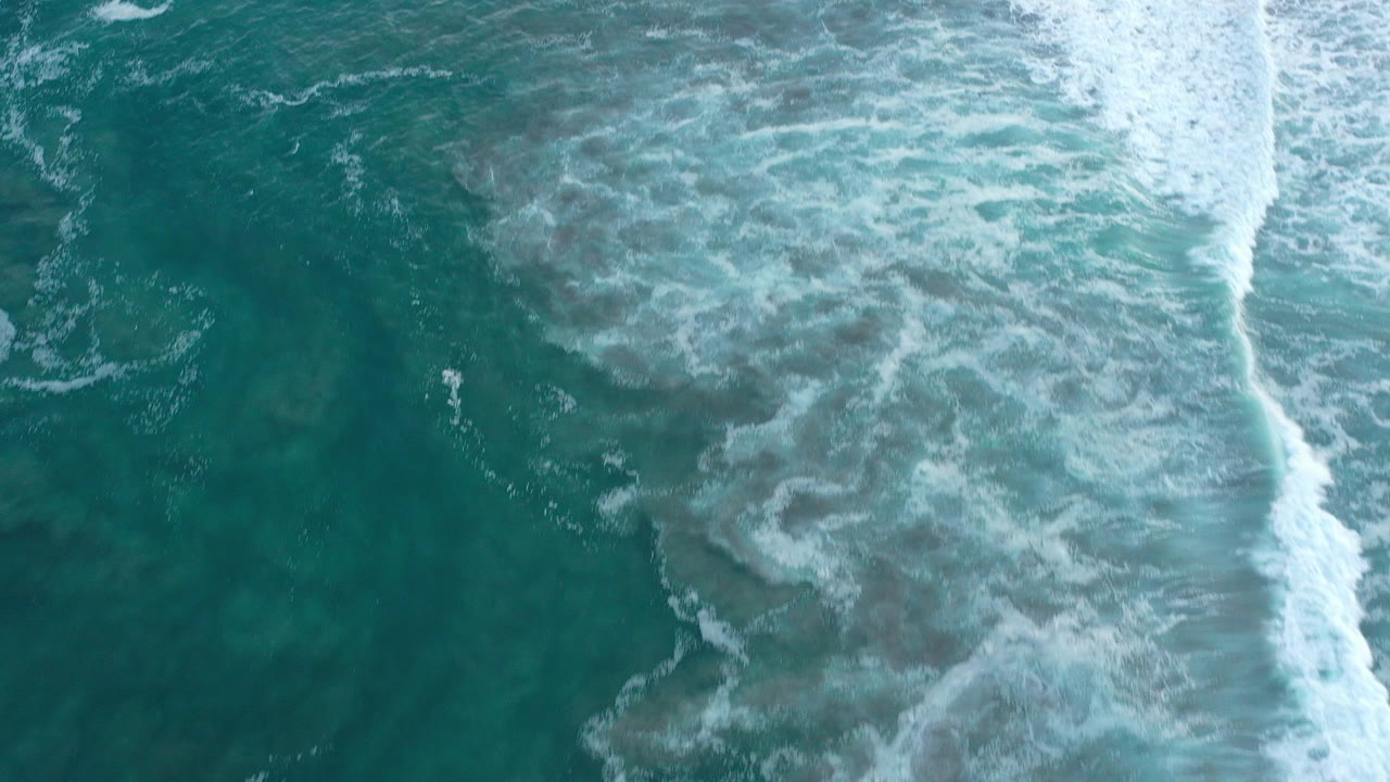 Overhead teal ocean with a diagonal band of white surf.