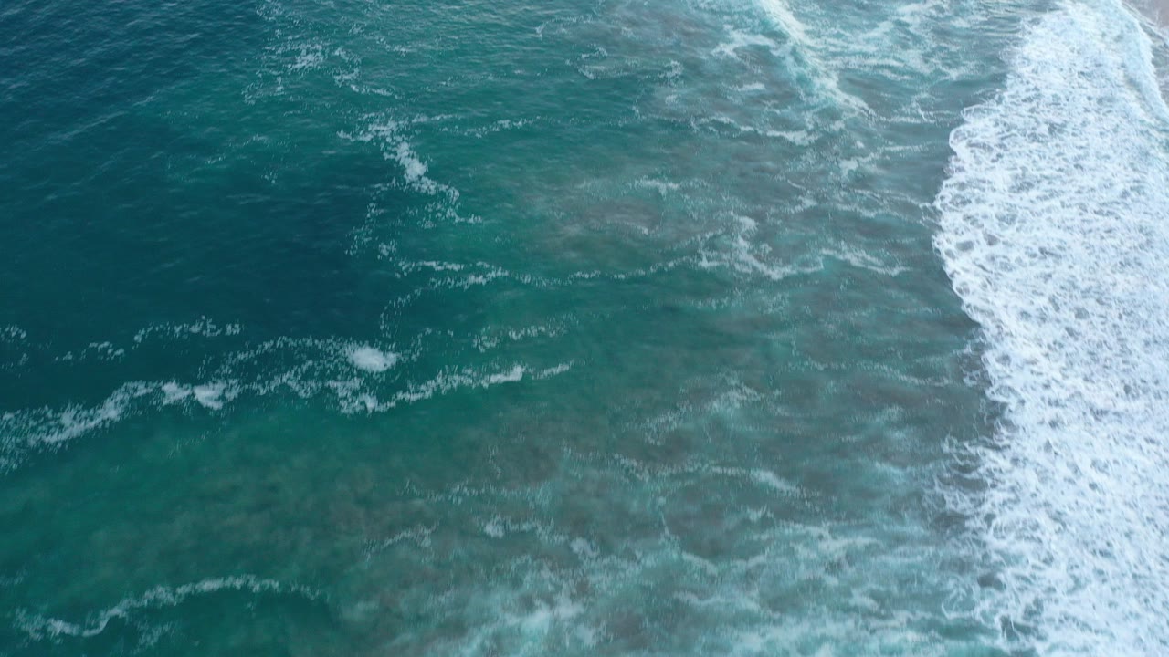 Top-down view of teal-green ocean and white surf foam along the right side in San Jose del Cabo, Mexico, with no visible people.