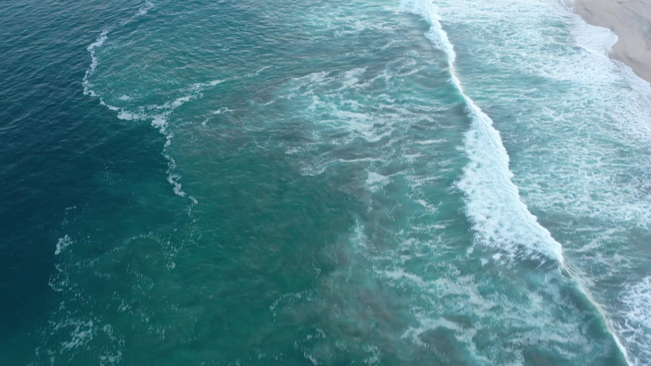 Ocean foam patterns beside an empty sandy shoreline