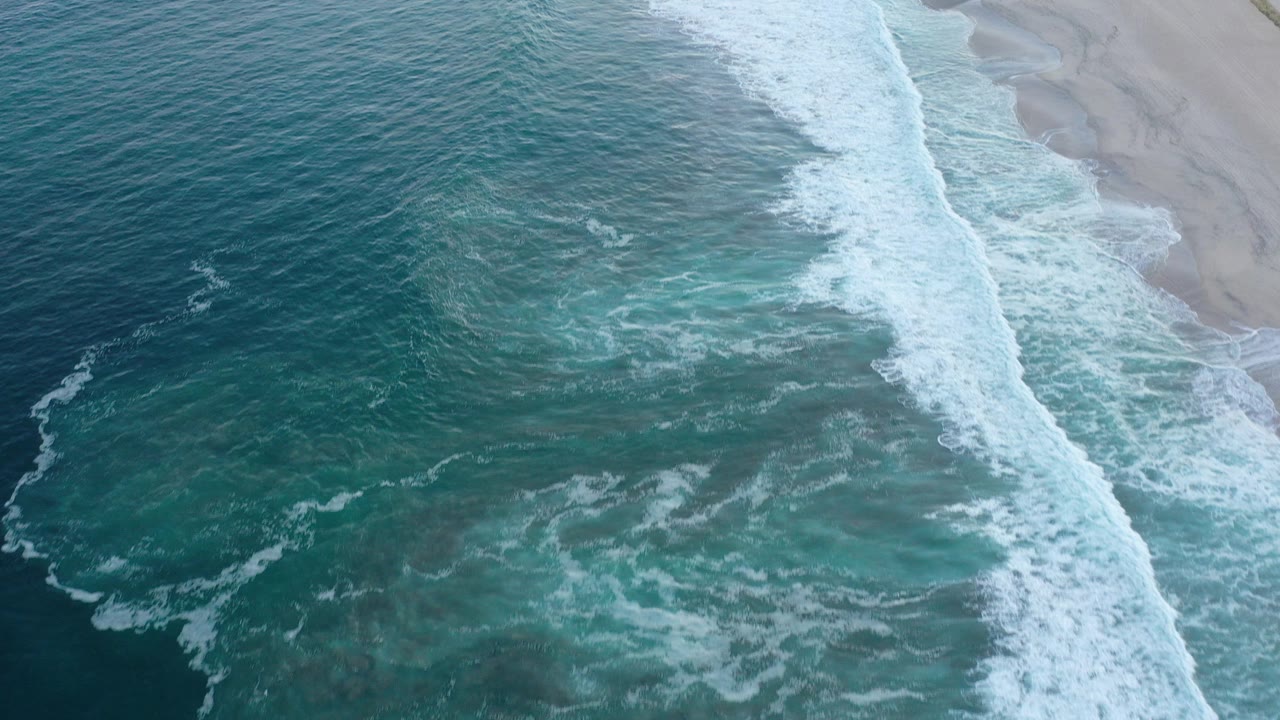 Aerial view of teal ocean waves breaking onto a sandy beach.