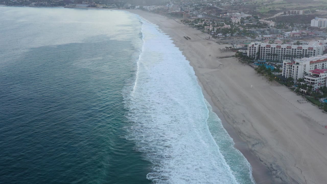 Aerial view of surf beside a wide beach and resort buildings