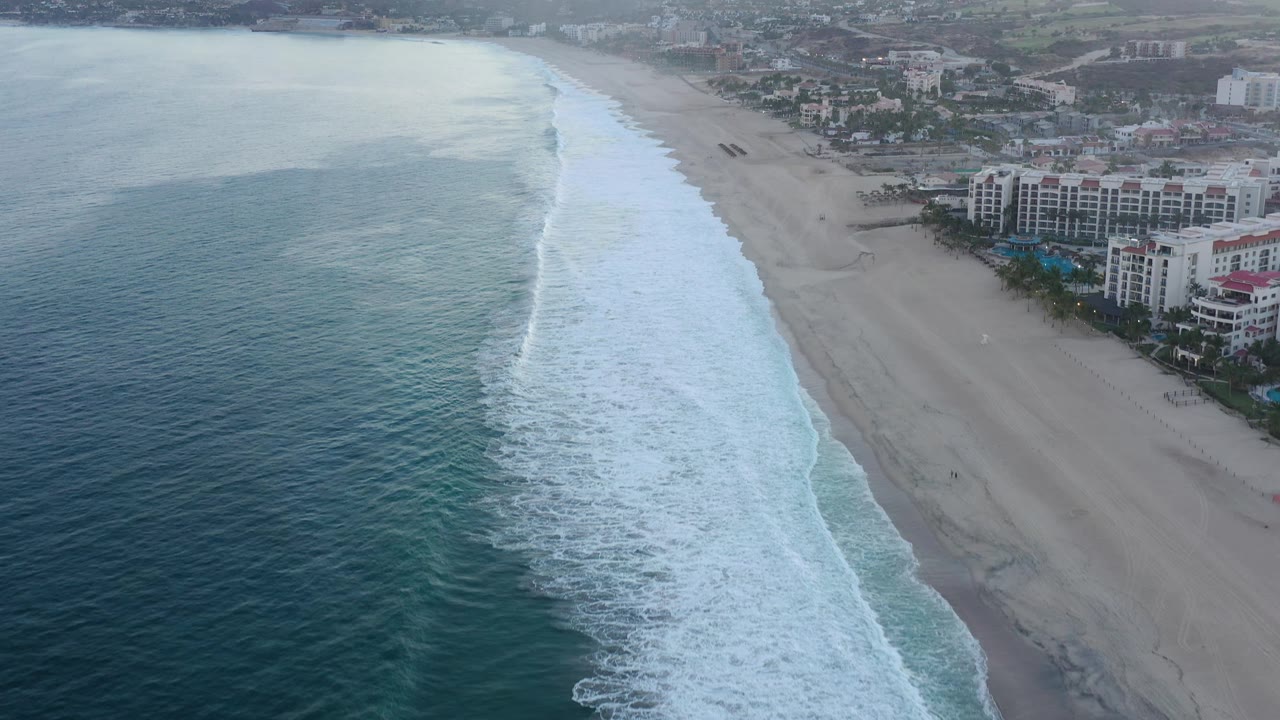 The second frame keeps the ocean on the left while white surf advances along the San Jose del Cabo beach, with beachfront resort blocks and no visible people.