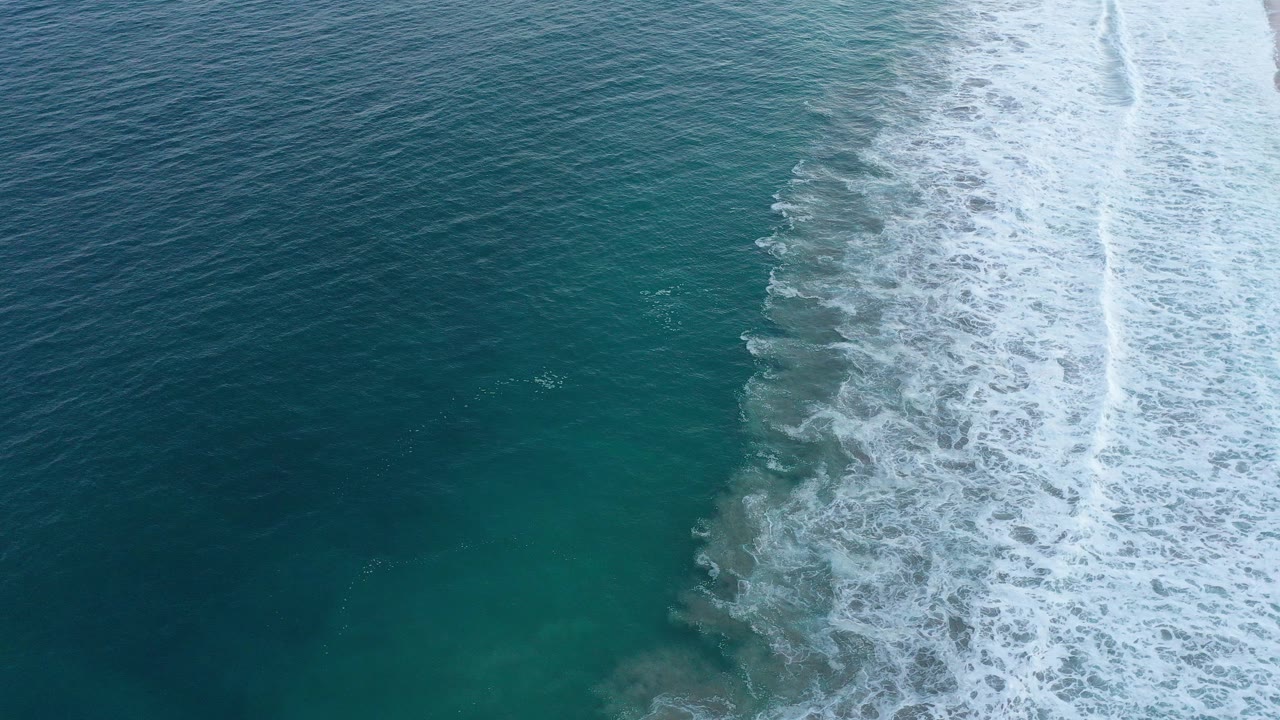 Overhead view of blue-green ocean and white surf foam along the San Jose del Cabo shoreline, with no visible people.
