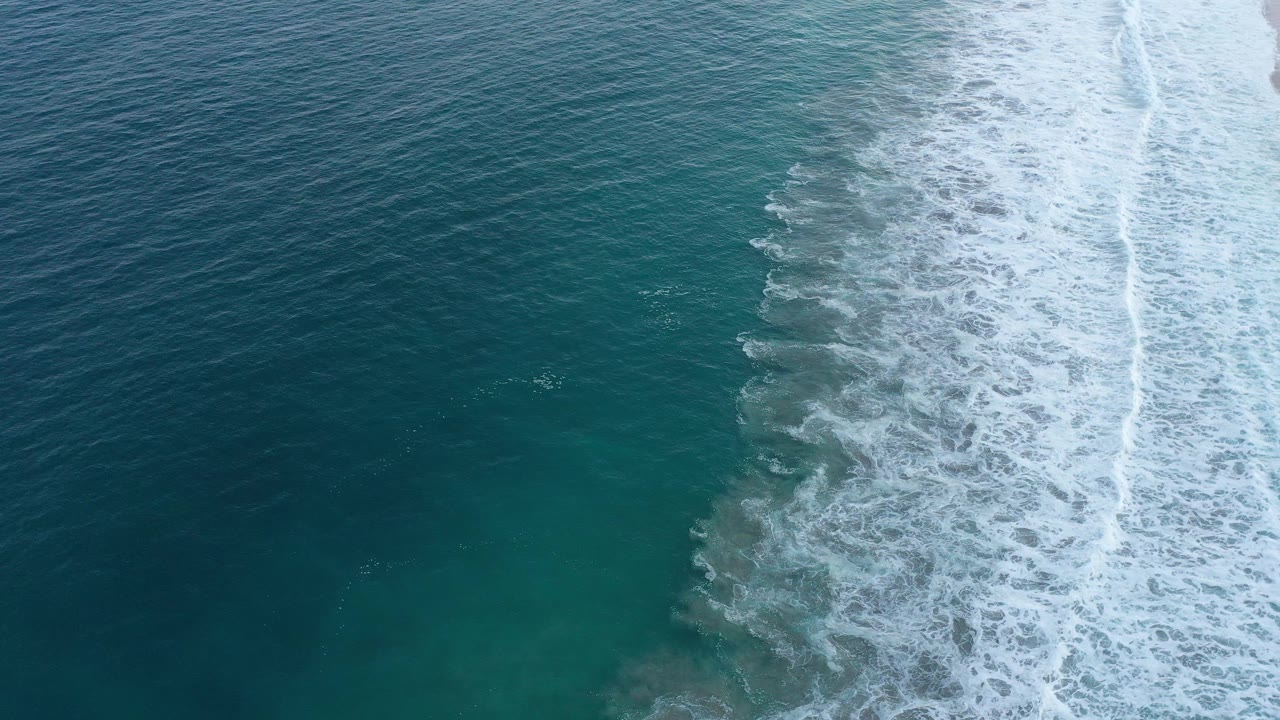 Foamy surf forms a bright vertical band between deep water and shoreline.