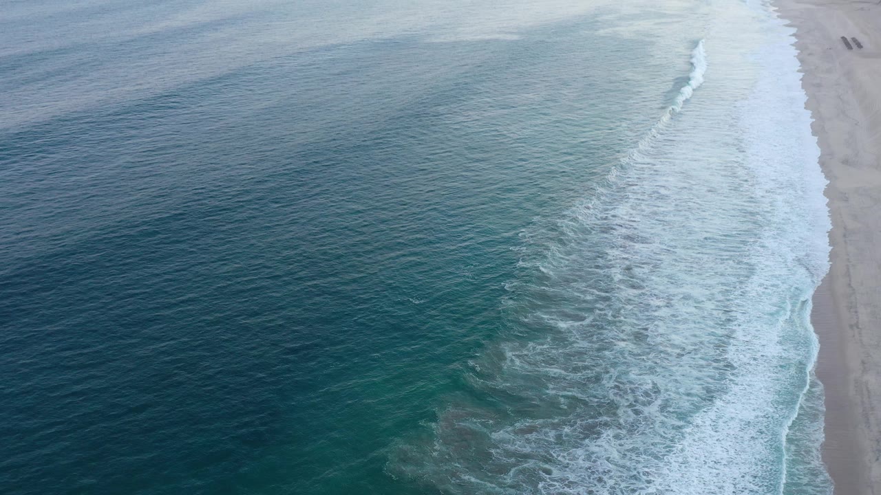 High aerial shoreline with breaking surf and beach at frame edge.