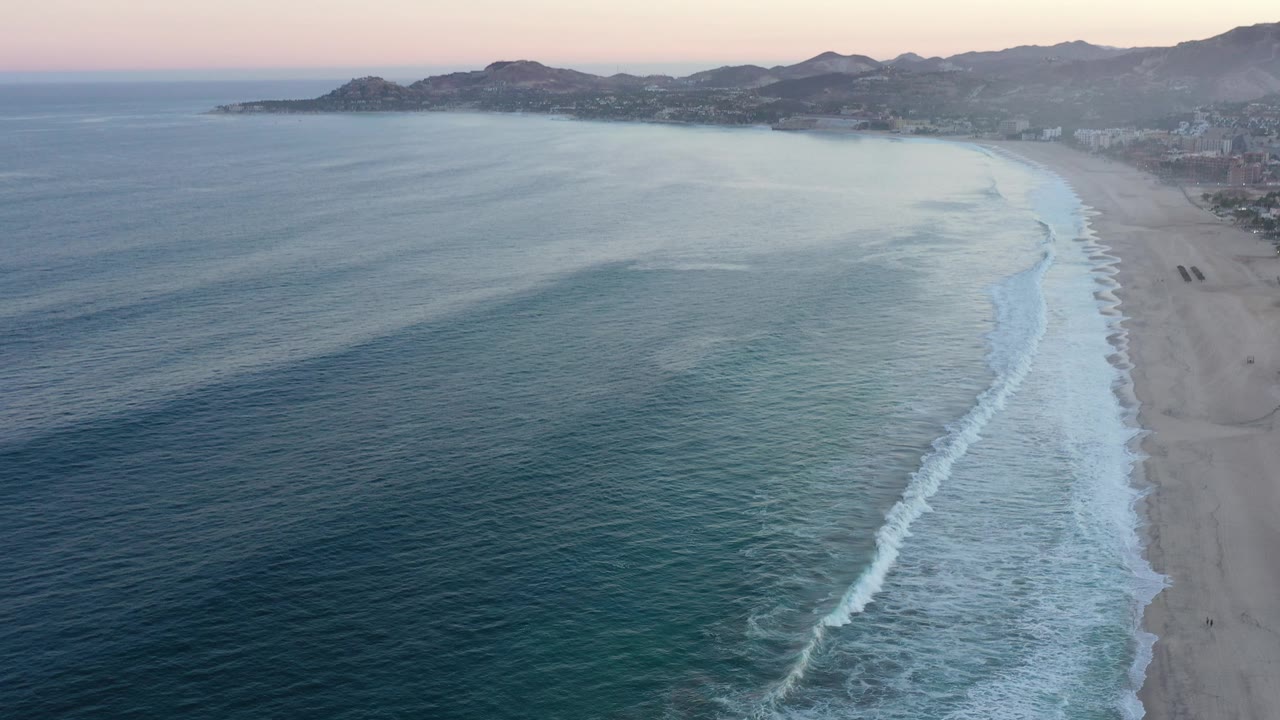 Curved beach and calm ocean seen from above near sunset.