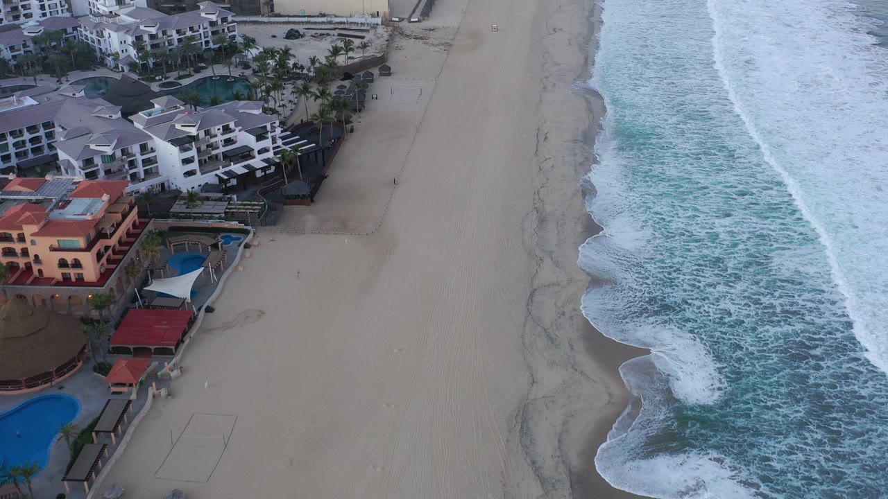 Aerial view of beachfront buildings beside sand and surf.