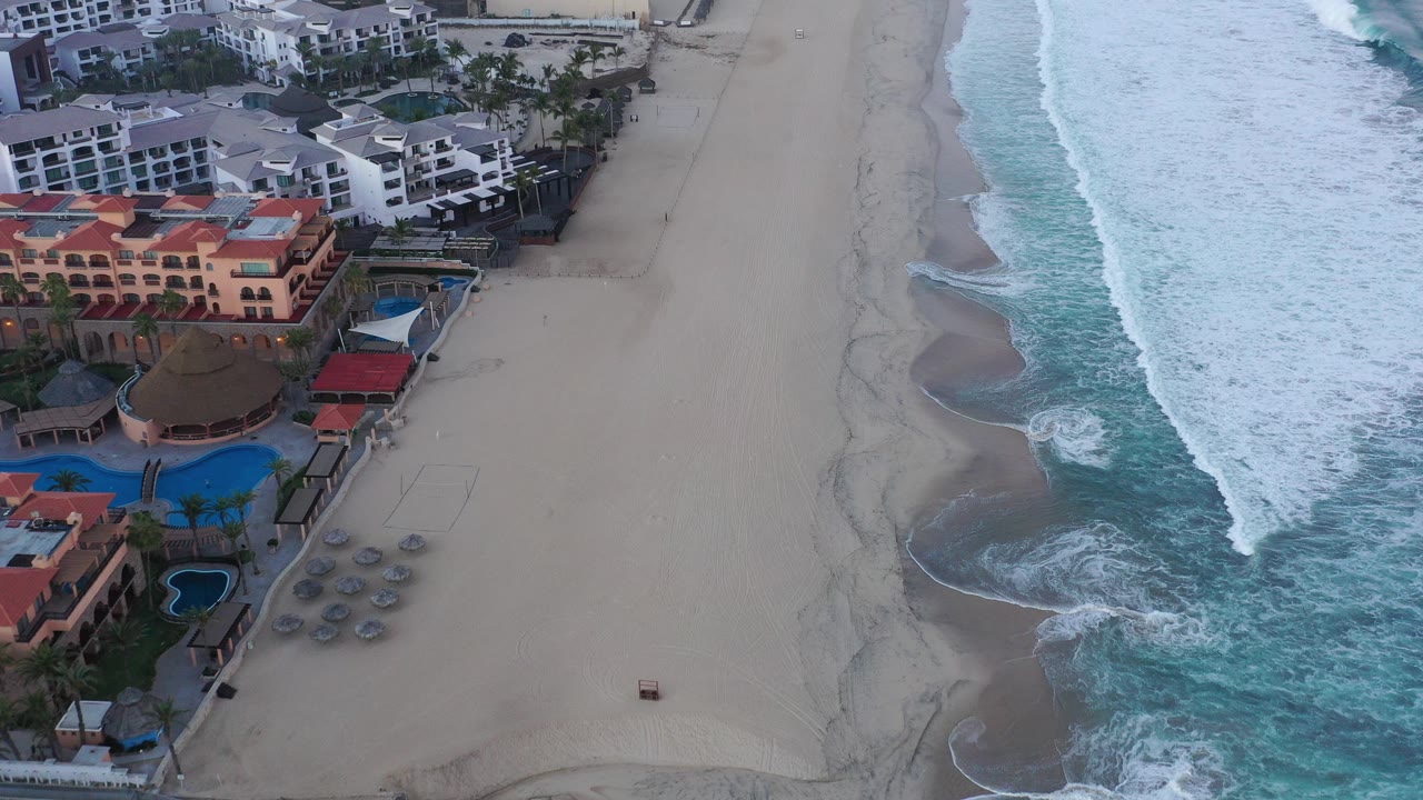 Aerial view of resort buildings beside a sandy beach and surf.