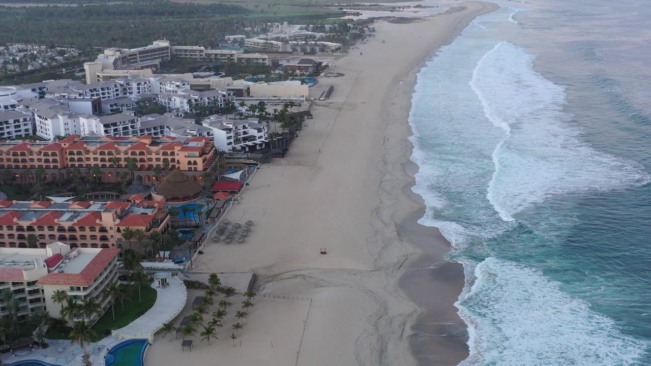 Aerial view of beachfront buildings beside a wide sandy shoreline and breaking surf.