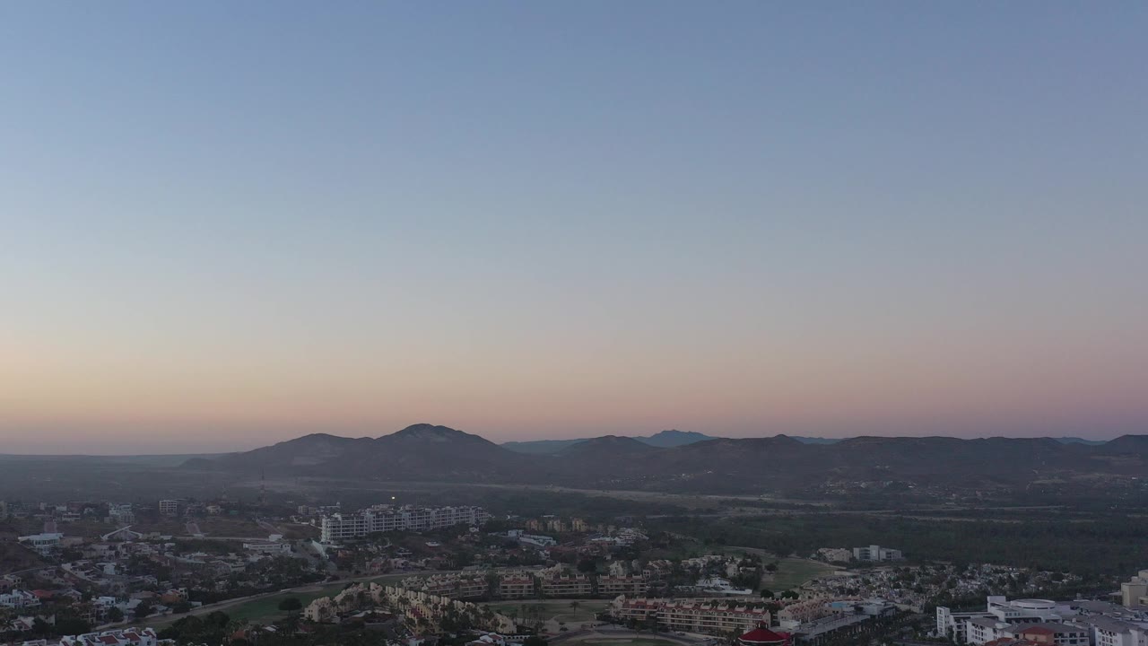 Elevated city view under a pale dusk sky with hills on the horizon.