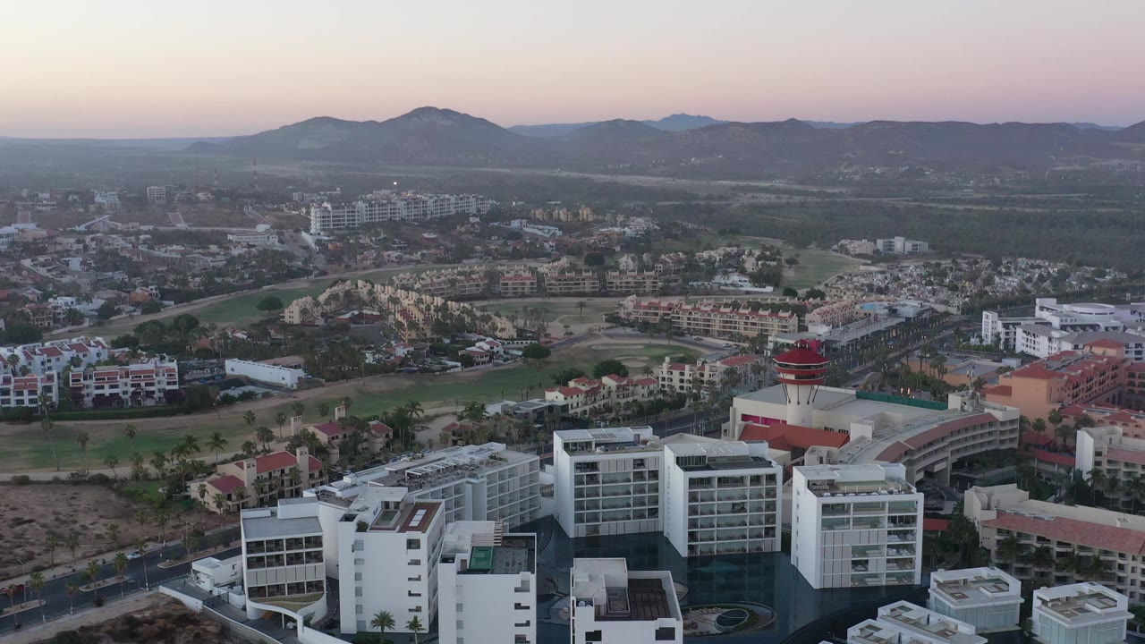 Aerial view in San Jose del Cabo, Mexico, with the red-roofed tower near the lower right, white buildings in front, gridded roads in the valley, and no visible people.