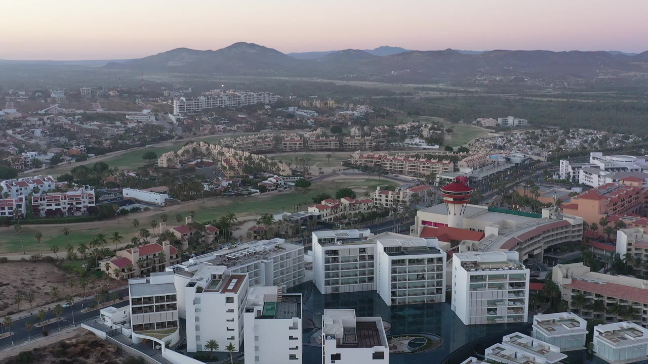 Wide drone-like view of buildings, green corridors, roads, and mountains.