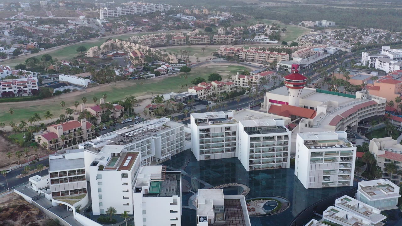 Aerial view of white hotel or condo buildings around a dark pool courtyard.