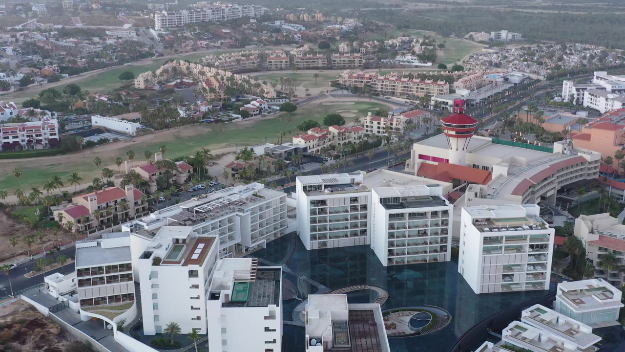 Aerial view in San Jose del Cabo, Mexico, showing the white hotel or condo complex slightly farther along the pass, with villas and landscaped open space in the background and no visible people.