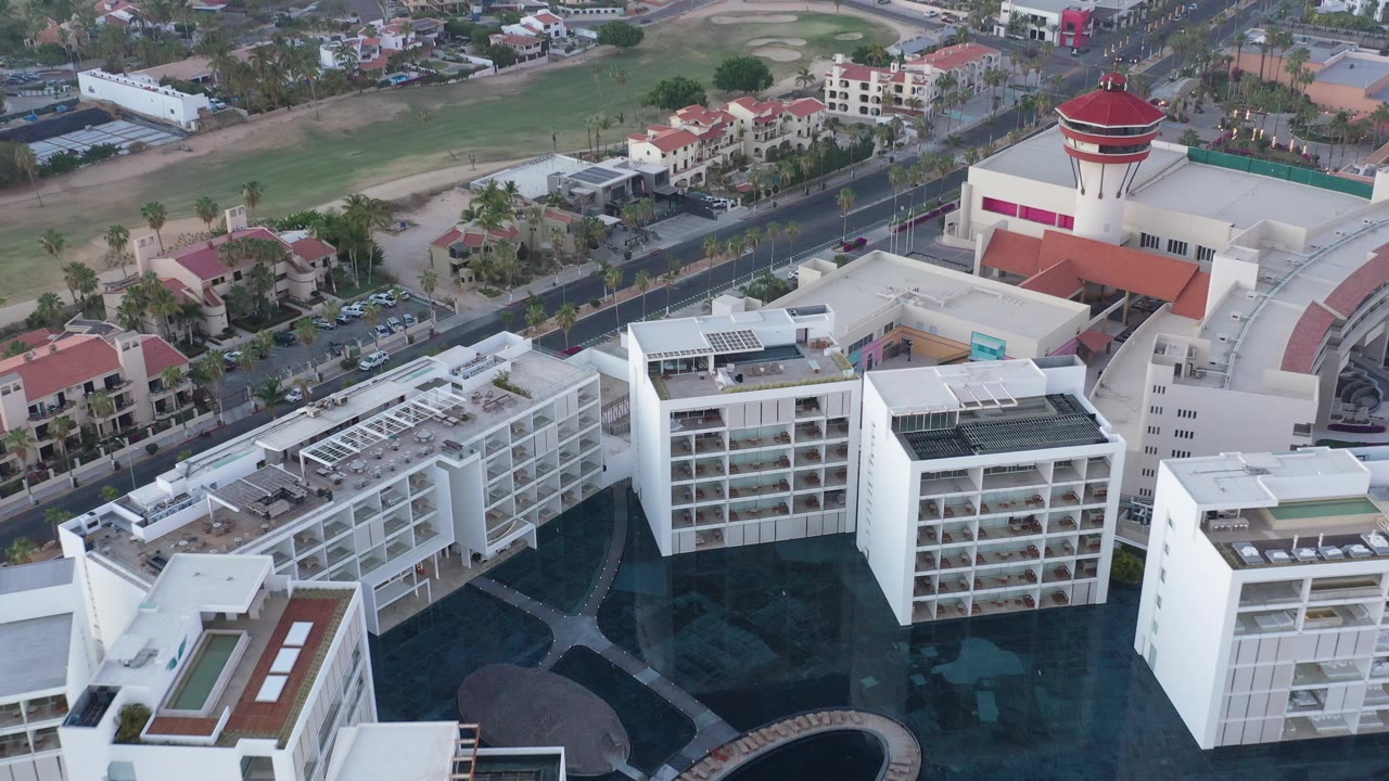 Elevated view of white buildings, road, houses, and open green ground.