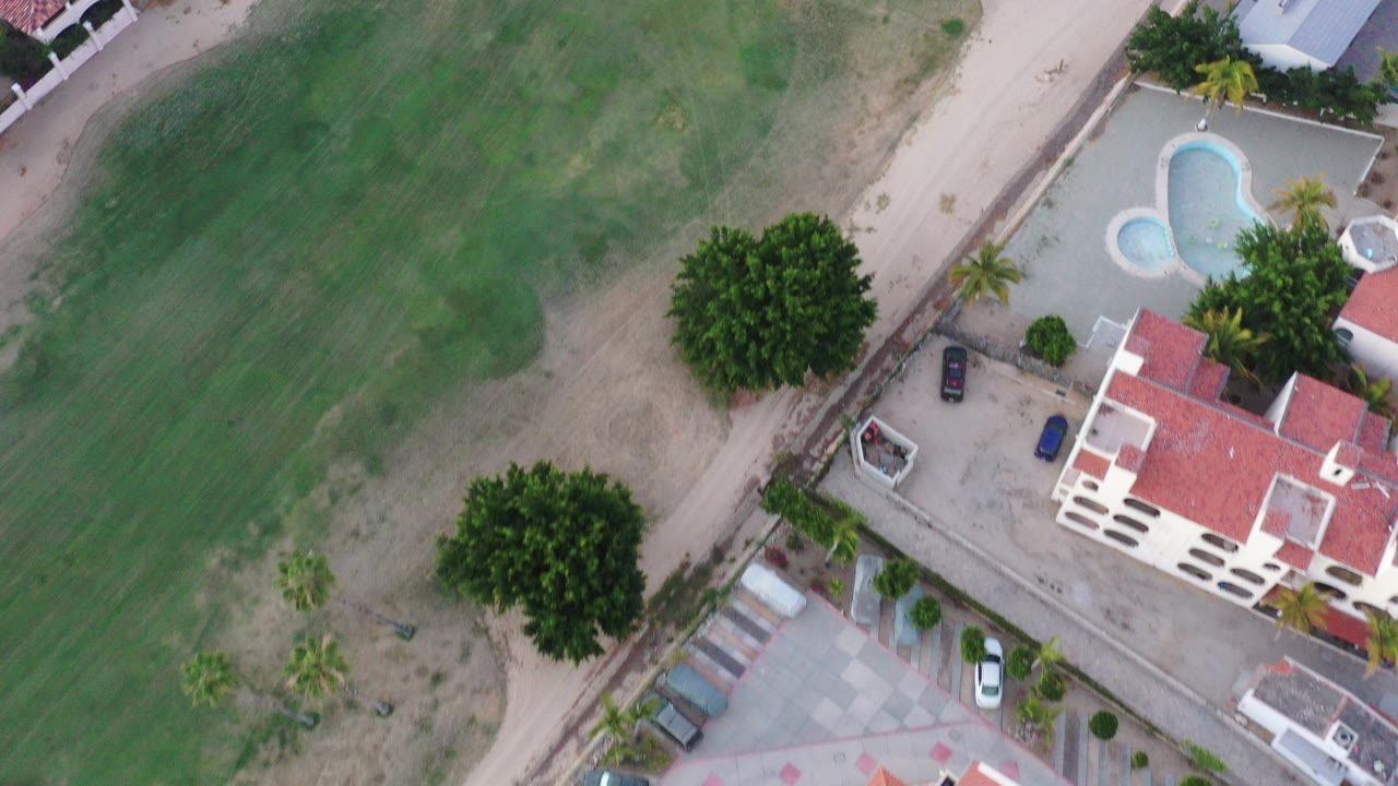 Overhead view of a golf fairway beside red-roofed homes and a pool.
