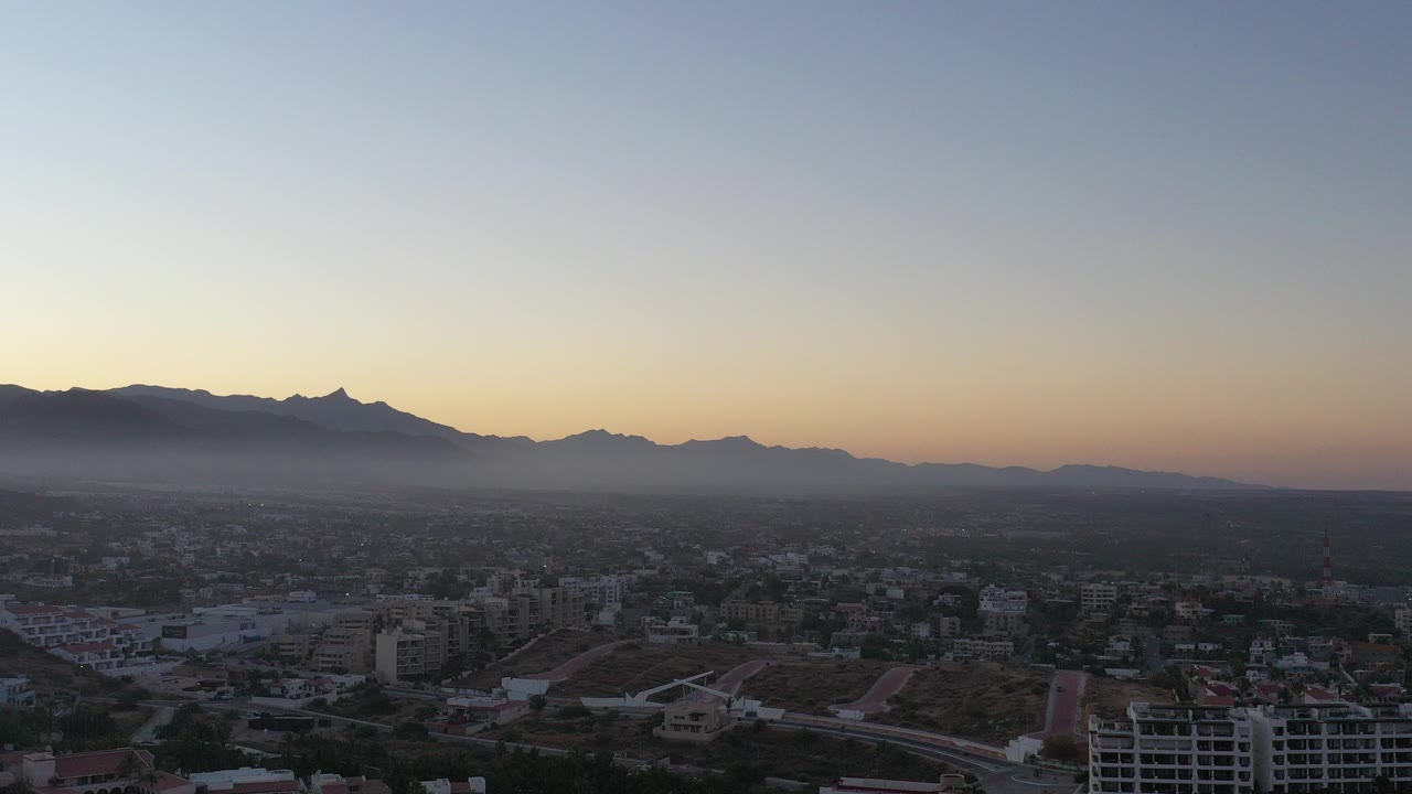 Wide elevated town view below hazy mountains at low light