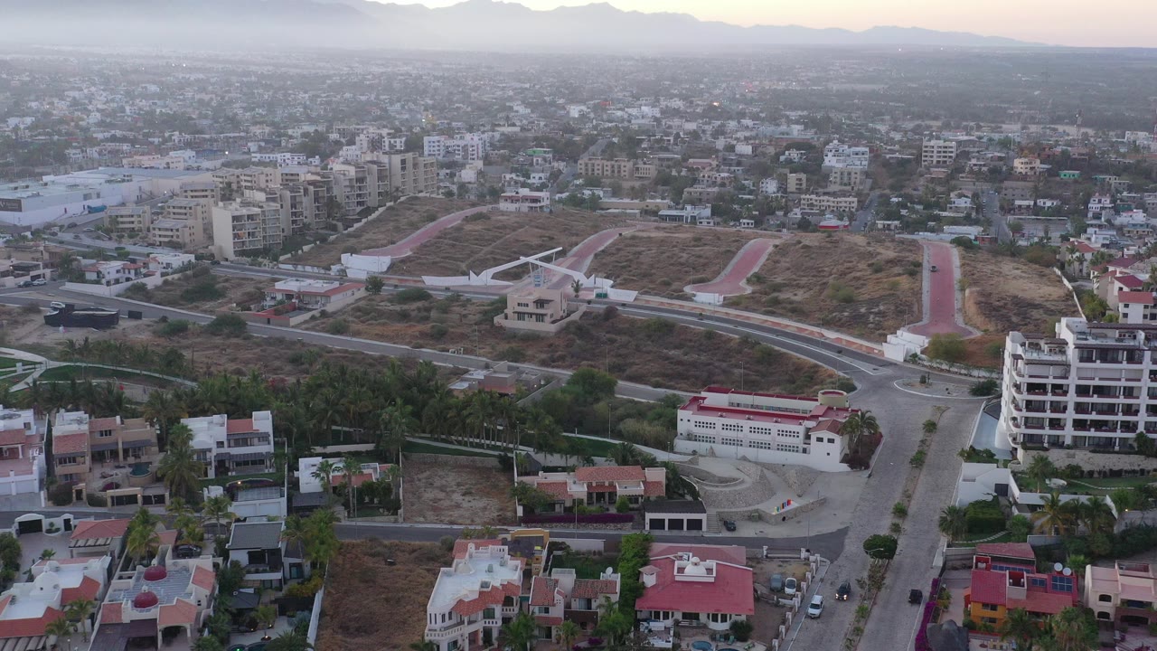Aerial view over roads, houses, hillside paths, and distant city buildings.