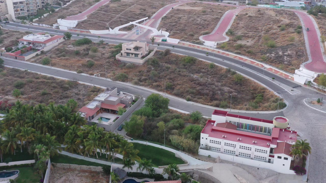 Aerial view of curved roads, dry hillside, palm trees, and red-roofed buildings.