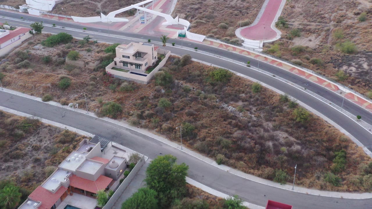 Overhead view of curving roads, dry hillside, and a pale house with a pool.