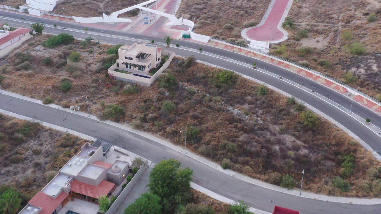 Aerial frame in San Jose del Cabo centers a pale hillside residence between empty roads, scrubby terrain, red sidewalk sections, and no visible people.