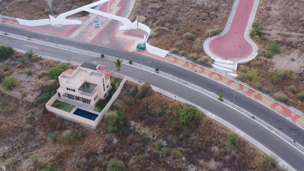 Aerial view of a curved road, red paved plaza, white canopy, and small building.