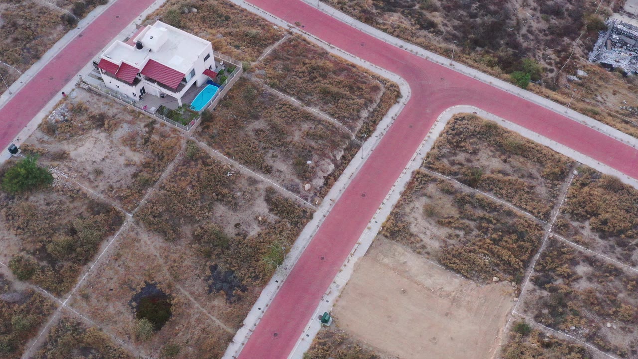 Aerial view of a house, pool, red road, and dry fields.